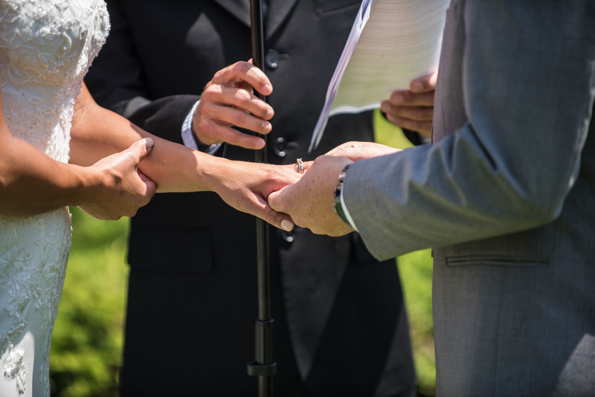 Groom slides diamond ring onto his bride's finger as official looks on during wedding ceremony at alter.