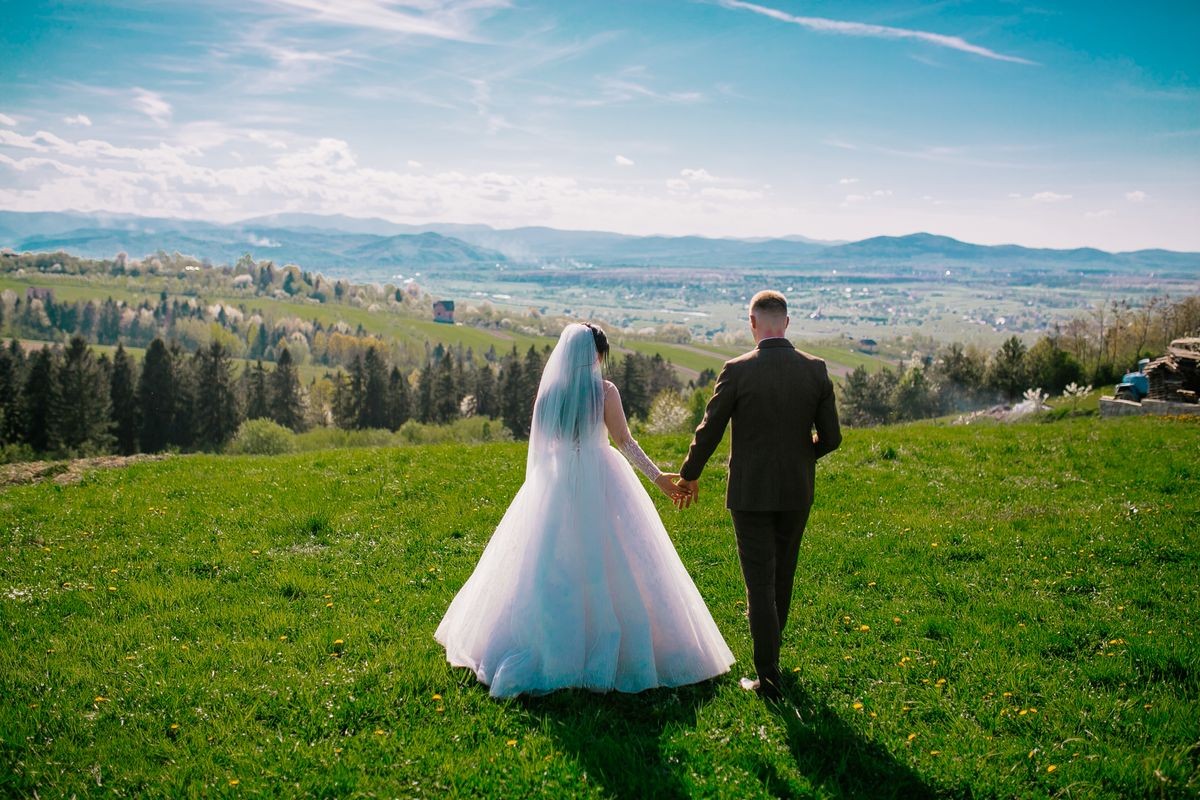 Newlyweds on the wedding day.
Walking with a mountain lawn. Carpathian Mountains in the background. follow me photo. Bride and groom hug each othe before wedding ceremony.