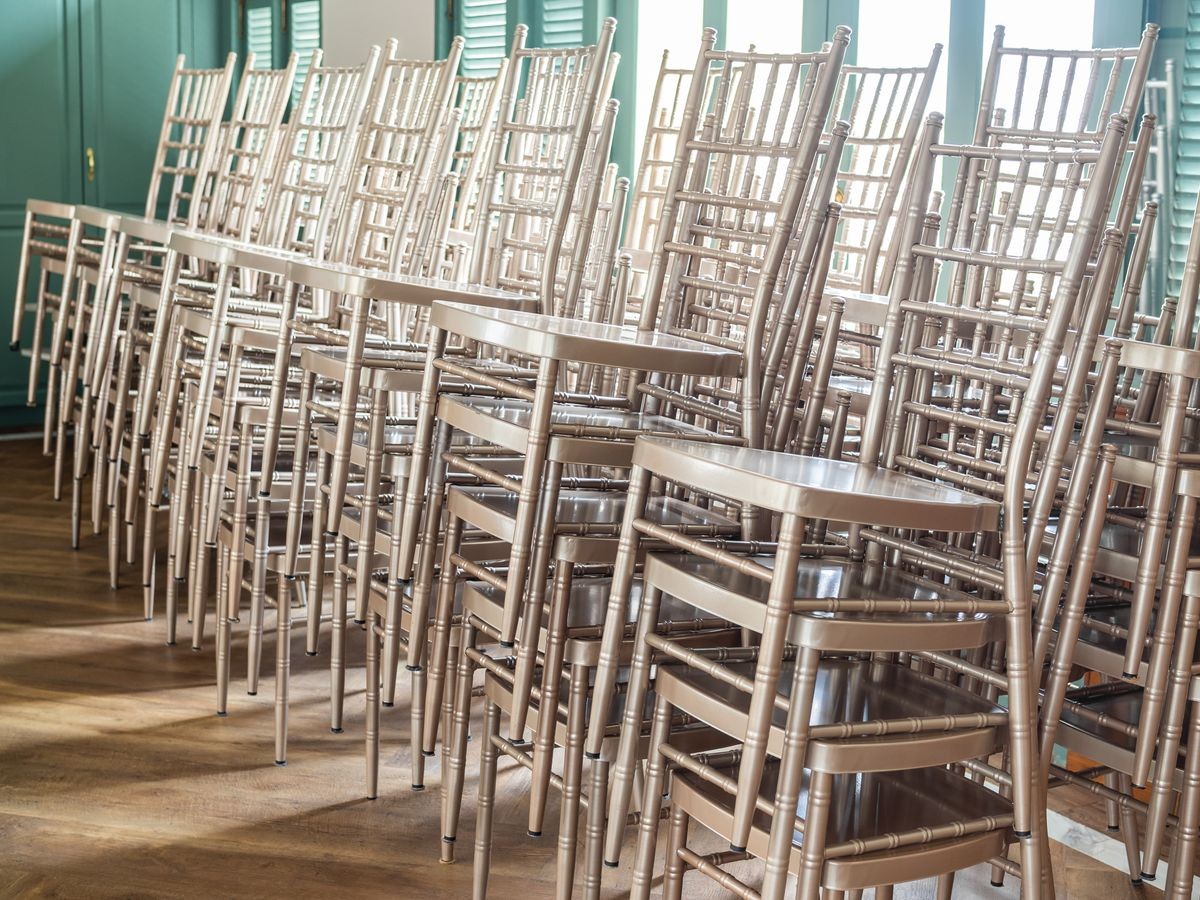 Rows of modern stacked silver chairs on wooden floor with the light from outside with the green wooden windows glass.